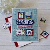 Handmade greeting card with postage stamps and envelopes on it with sending paper hugs sentiment on it.