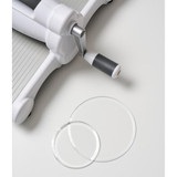 Two clear circular die cutting plates on a white table next to a die cutting machine. Two clear circular die cutting plates on a white table next to a die cutting machine.