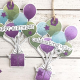 Two handmade greeting tags with balloons holding a present up with celebrating you sentiment on it.