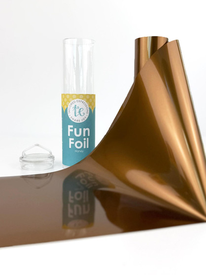 Taylored Expressions TE Fun Foil - Honey featuring a shiny, warm golden-brown metallic foil sheet unrolled beside its teal storage tube.