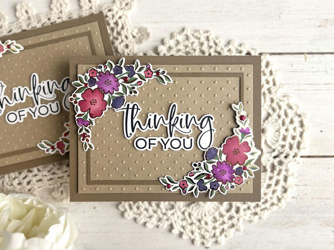 Handmade greeting card with flowers on it and thinking of you sentiment on it with a card in background.