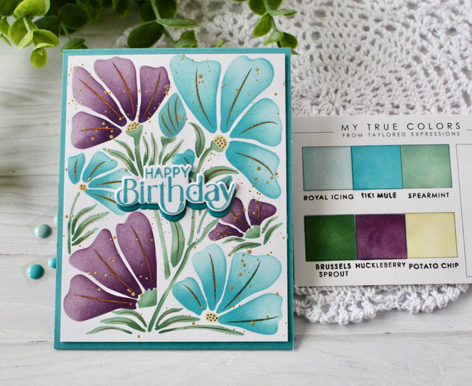 Handmade greeting card with flowers on it and happy birthday sentiment on it with crafting materials in background.