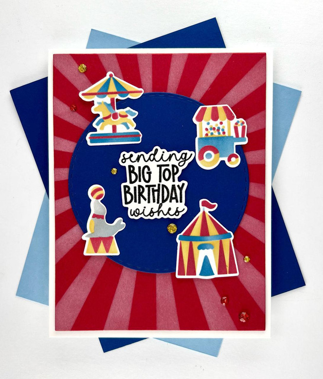 Handmade greeting card that is carnival themed with sending big top birthday wishes sentiment on it with cardstock in background.