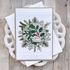 Handmade Christmas greeting card featuring a circular arrangement of evergreen branches, holly leaves, and berries with a festive sentiment in the center.
