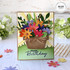Handmade greeting card with flowers in a pail with happy birthday sentiment on it and flowers in background.