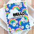 Handmade greeting card of rainbows and flowers and hello friend sentiment with cardstock in background.