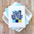 Handmade greeting card with colorful squares and happy birthday sentiment on it with cardstock in background.
