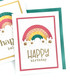 Handmade greeting card with rainbow and happy birthday sentiment with cards in background.