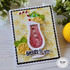 Handmade greeting card with a drink cup, citrus fruit, and cheers to you sentiment on it with flowers in the background.