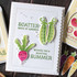 Handmade greeting card with two peas and scatter seeds of kindness sentiment on it and a radish with wishing you a beautiful summer sentiment on it with crafting materials in the background.