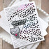 Handmade greeting card with foiled heart rays on it with cat holding heart and delivering loads of love sentiment on it with cardstock in background.