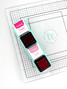 Image of Glassboard Buddy - Mini Ink Cubes which is a magnetic tray that holds mini ink pads and in the picture there is an example of two mini inks with the lids off. Image of Glassboard Buddy - Mini Ink Cubes which is a magnetic tray that holds mini ink pads and in the picture there is an example of two mini inks with the lids off.