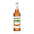 A 750 mL (25.4 fl oz) glass bottle of Monin Praline Premium Gourmet Syrup. The amber-colored syrup is contained in a clear bottle with a white label featuring the Monin logo and illustrations of pecans, green nut husks, and vanilla beans. The label includes the text "Praline" and "Premium Gourmet Syrup."