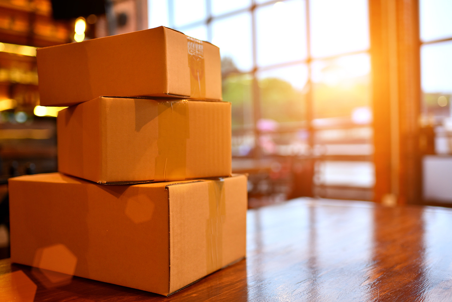 Photo of unmarked, cardboard boxes stacked on a table in a sunset-lit room.