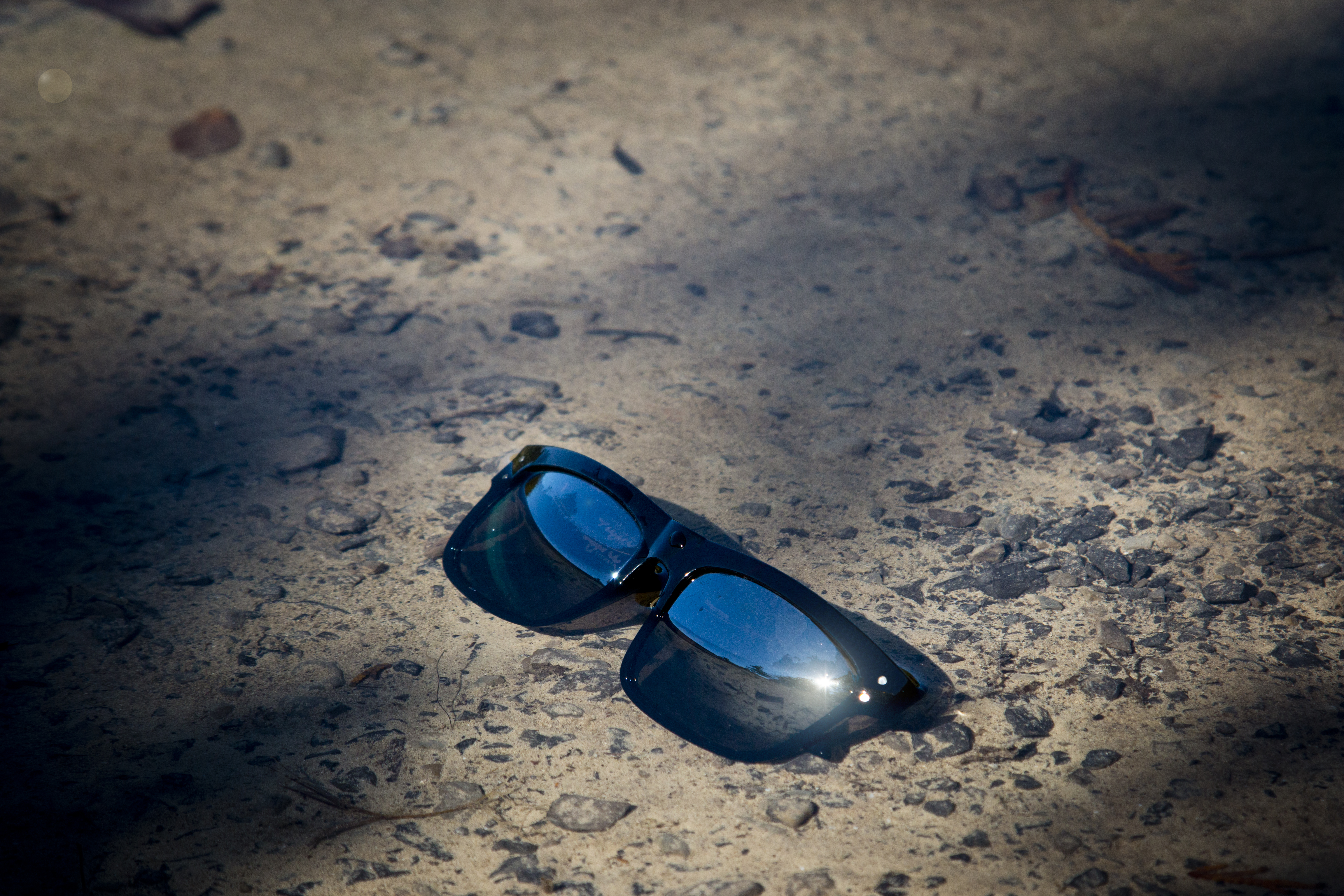 Black sunglasses with mirrored lenses resting on gravel in the sun