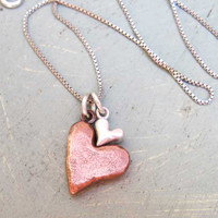 Hand sculpted copper and silver hearts nested together on a silver chain, shown from the top 