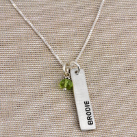 Side view of custom sculpted silver long rectangle, personalized with hand stamped name Brodie and green birthstone