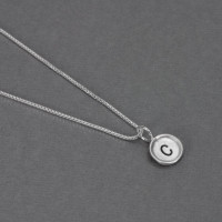 Side view of custom mini round initial charm, handmade in sterling silver and personalized with hand stamped initial "C", on silver box chain
