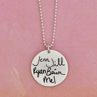 Custom silver necklace for Nana/Grandma, personalized with multiple grandkids' handwritten signatures on a 7/8" silver disc, hung on a silver ball chain, shown on pink background