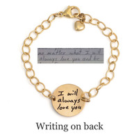 Personalized gold disc bracelet, with the back side of disc custom engraved with husband's handwritten "I will always love you". Charm is on a gold chain, with a gold puffed heart charm attached to the clasp. Shown with the original handwriting on a white background