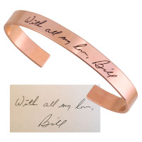 Custom rose gold handwriting memorial cuff bracelet, engraved with the signature of a loved one, shown with the handwritten note used to personalize it on white