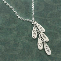 Custom Silver Cascade Necklace, hand stamped with the word love and hearts, shown close up on green