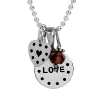 Personalized silver disc and silver heart necklace, hand stamped with dotted border and the word love, with a garnet birthstone, shown close up on white