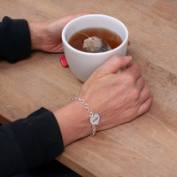 Model wearing silver Full Heart Bracelet, personalized with "Ethan", holding cup of tea