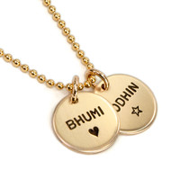 Hand stamped custom Gold Name Discs necklace personalized with kids' names, shown from the side on white