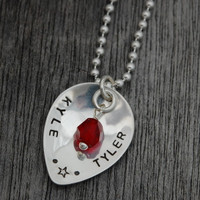 Custom silver Scooped Teardrop with Stone Necklace, personalized with hand stamped Kyle and Tyler and a star, and a red crystal birthstone, shown close up on wood