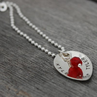 Side view of custom silver Scooped Teardrop with Stone Necklace, personalized with hand stamped Kyle and Tyler and a star, and a red crystal birthstone, shown on wood 