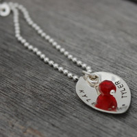 Side view of custom silver Scooped Teardrop with Stone Necklace, personalized with hand stamped Kyle and Tyler and a star, and a red crystal birthstone, shown on wood