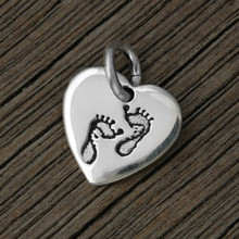 Sterling silver heart charm, with Baby Feet stamped on the front, shown on wood background