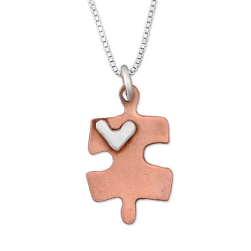 Handmade copper puzzle piece charm with silver heart on a necklace, shown close up on white