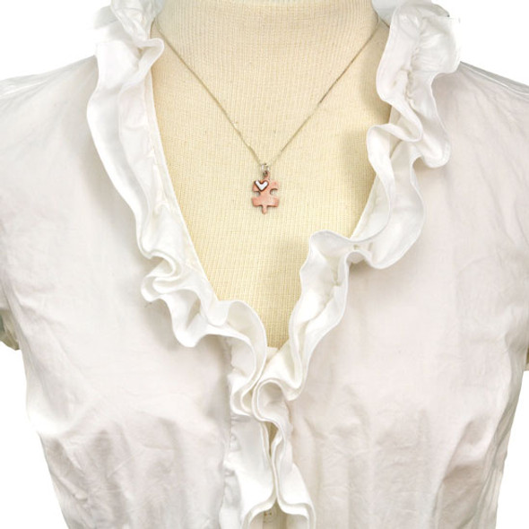 Handmade copper puzzle piece charm with silver heart on a necklace, shown on a model