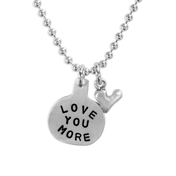 Silver necklace Hand Stamped with the words Love You More , and a silver heart charm, shown on white, close up