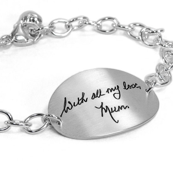 Custom silver oval handwriting bracelet, with actual handwriting, shown from side on white. close up