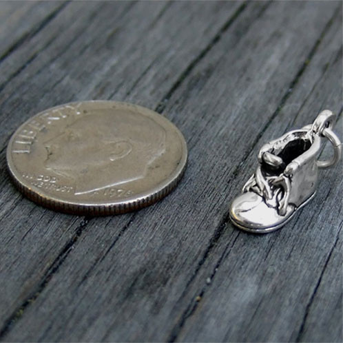 Sterling silver Baby Shoe Charm, shown on wood with a dime for size context