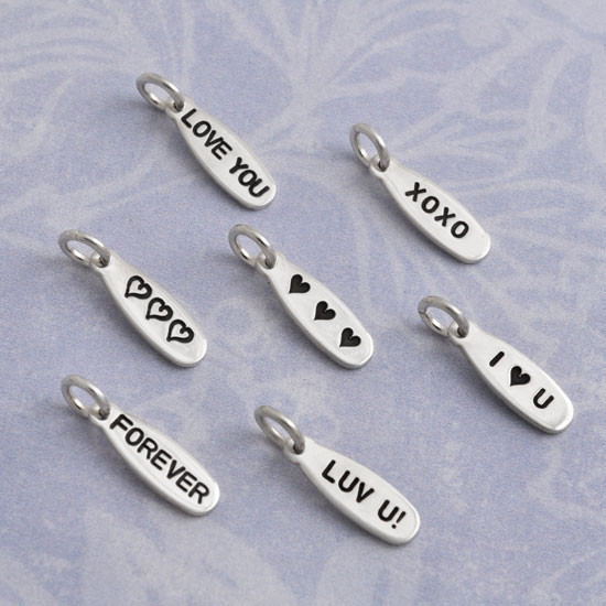 A collection of silver Lil Love Tags, personalized with various messages stamped on them, including Love You, Forever, Luv U!, XOXO, I heart you