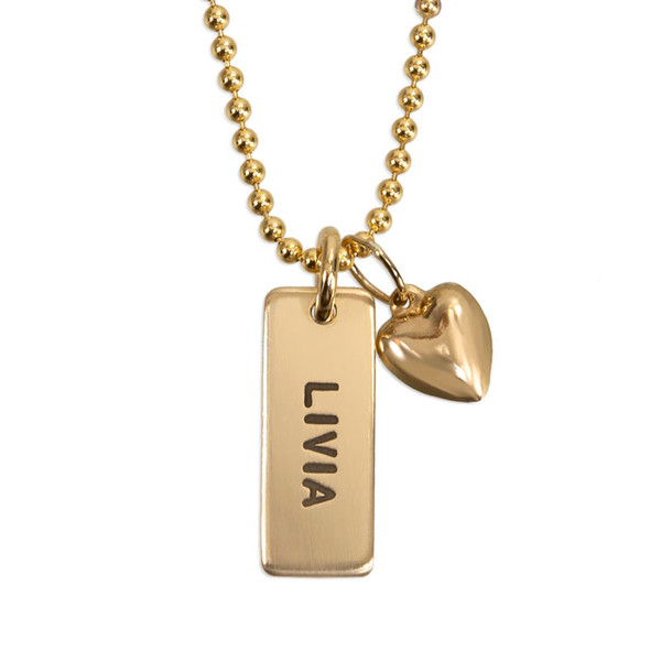 Custom personalized gold necklace with rectangle charm for mom, hand stamped with child's name "Livia", with a puffed gold heart charm, shown close up on white