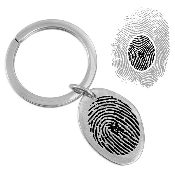 Handmade memorial silver oval key ring engraved with loved one's actual fingerprint,  shown with original print used to personalize it, on a white background
