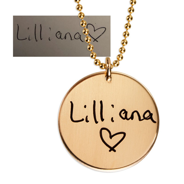 Custom gold disc handwriting necklace, personalized with daughter's handwritten signature "Lilliana (heart)", shown close up on white