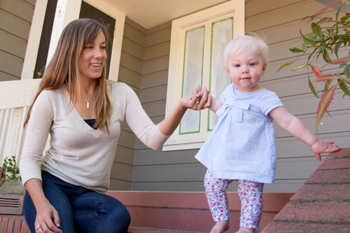 Mom wearing sculpted silver rectangle necklace with blue birthstone, playing with daughter, whose name is hand stamped on the necklace