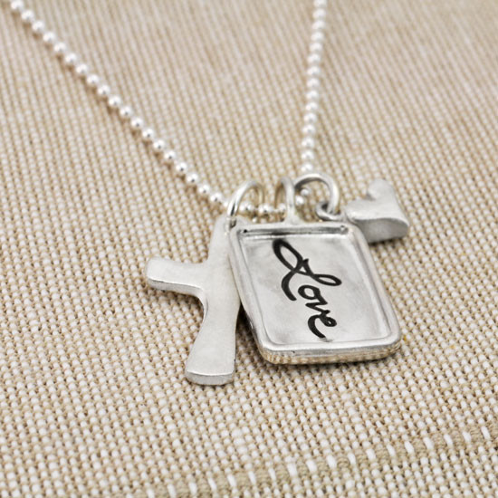 Silver charm with raised edge & the handwritten word Love, with a fine silver cross and fine silver heart, shown from the side