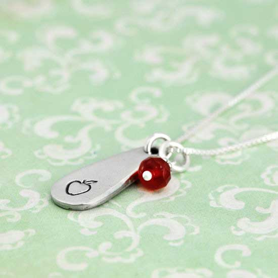 Thank you teacher gift. A  silver chain necklace with a teardrop shiny pewter charm and a red faceted birthstone representing an apple. Shown from the side