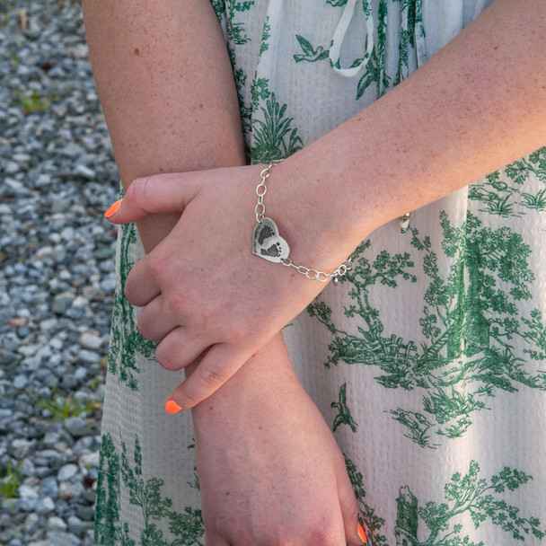 Model wearing custom silver heart bracelet personalized with child's actual footprints or handprints