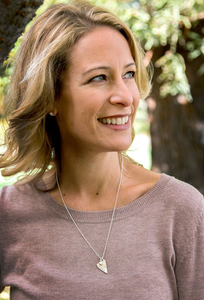 handmade long silver heart charm, hand stamped with a name, hung with a pearl , on a silver chain, shown on a white background, shown on a model