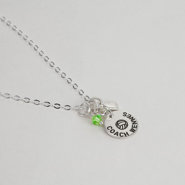Side view of custom silver circle charm necklace for a coach, personalized with volleyball and the coach's name, along with a team color birthstone and silver puffed heart charm. 