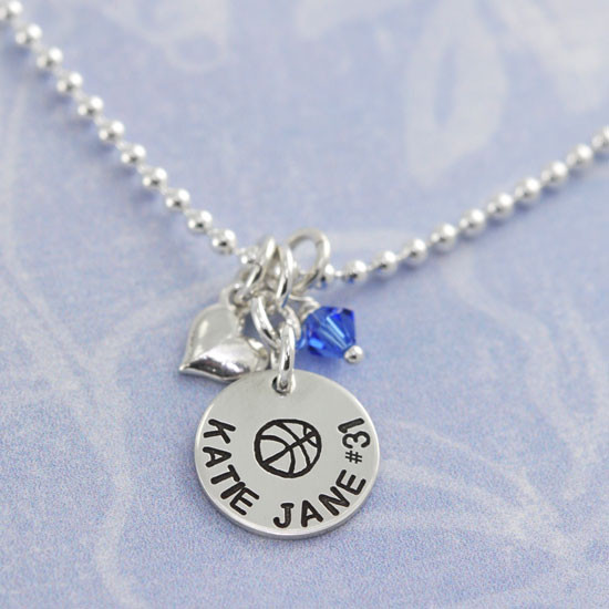 Custom team silver circle charm necklace for an athlete, personalized with basketball symbol, the player's name and number, along with a team color blue birthstone and silver puffed heart charm. 