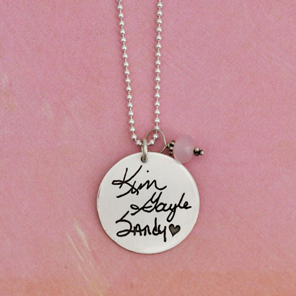 Personalized silver necklace for Mom, customized with 3 daughters' handwritten signatures on a 7/8" silver disc, hung with Opaque Pink Crystal Saucer Stone for June, on a silver ball chain, shown on pink background